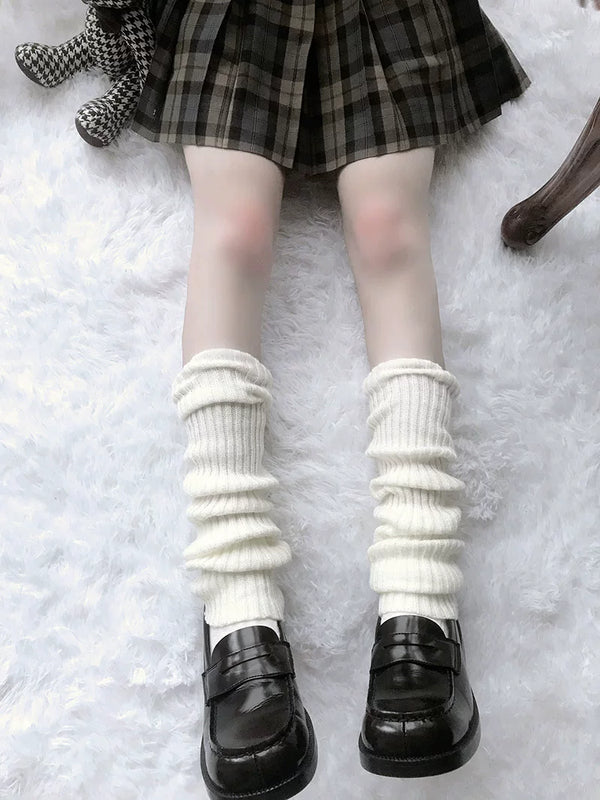 White ribbed knit leg warmers stacked above black platform shoes on a white textured surface.