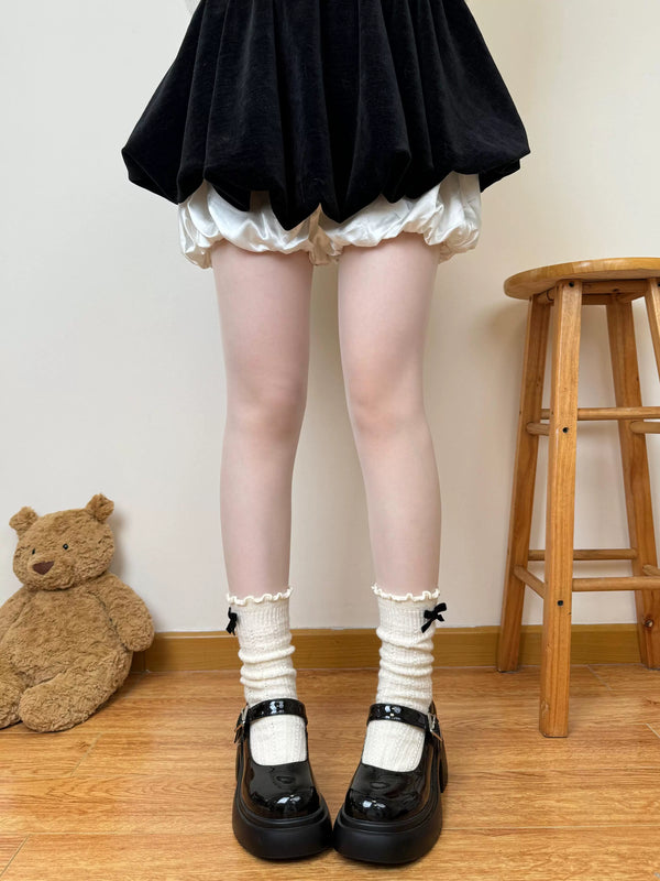 White thick slouch socks with a dark bow styled beneath a black skirt and patent Mary Jane shoes.