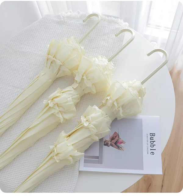 Cream lace-trimmed umbrellas arranged on a table, showing gathered ruffle details and hooked handles.