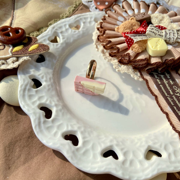 Chocolate-themed adjustable rings in assorted confection, heart, cat, teddy-bear and pastry designs displayed on a tray.