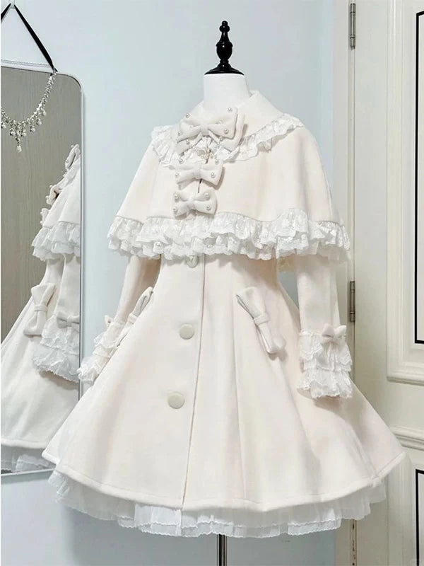 Ivory one-piece dress with a lace cape, bows and front buttons displayed on a dress form.