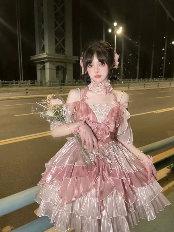 Pink JSK dress with a large bow and layered ruffles shown on a model at night.