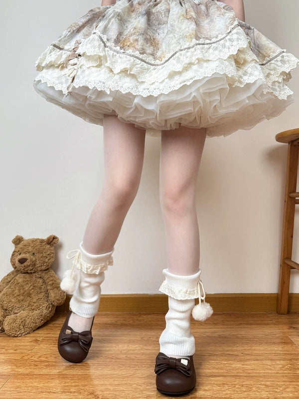 White knit slouch sock covers with lace trim, side ties and pom-poms worn with brown bow shoes.