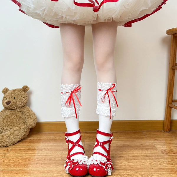 White lace-cuff socks with pink ribbon ties styled beneath a ruffled skirt.
