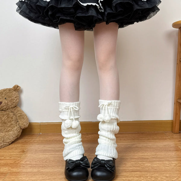 Slouchy ribbed leg warmers with drawstring pom-pom ties styled beneath a black ruffled skirt.