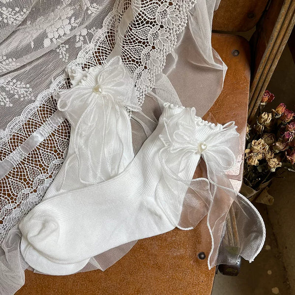 White ankle socks with oversized sheer bows and heart details worn with black shoes