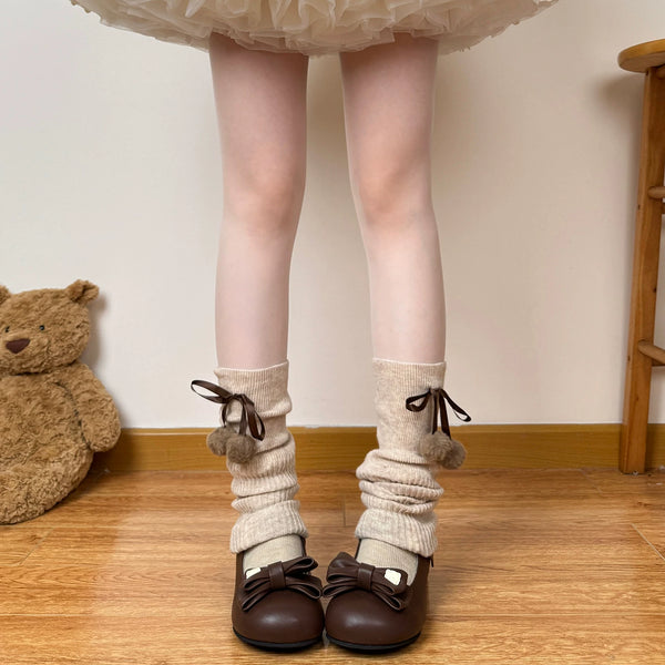 Cream knit scrunched leg warmers with brown ribbon ties and pom-pom accents
