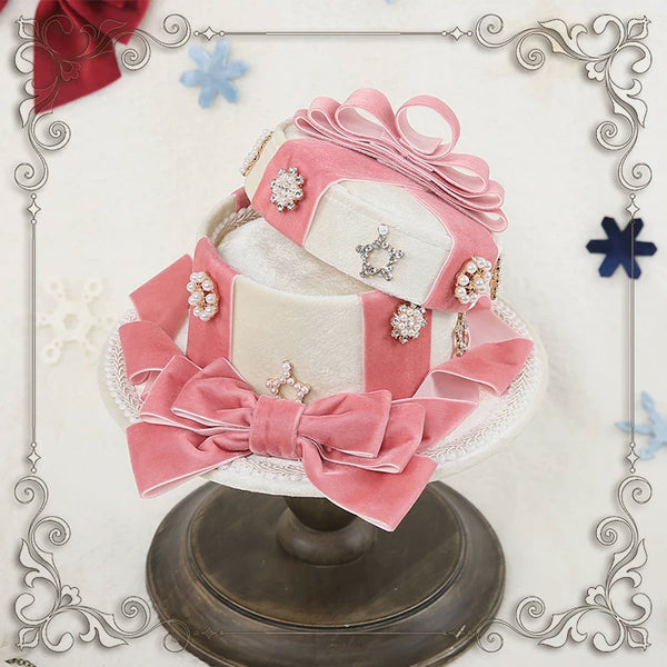 Pink-and-white velvet gift-box top hat with layered bows and jeweled accents on a display stand.