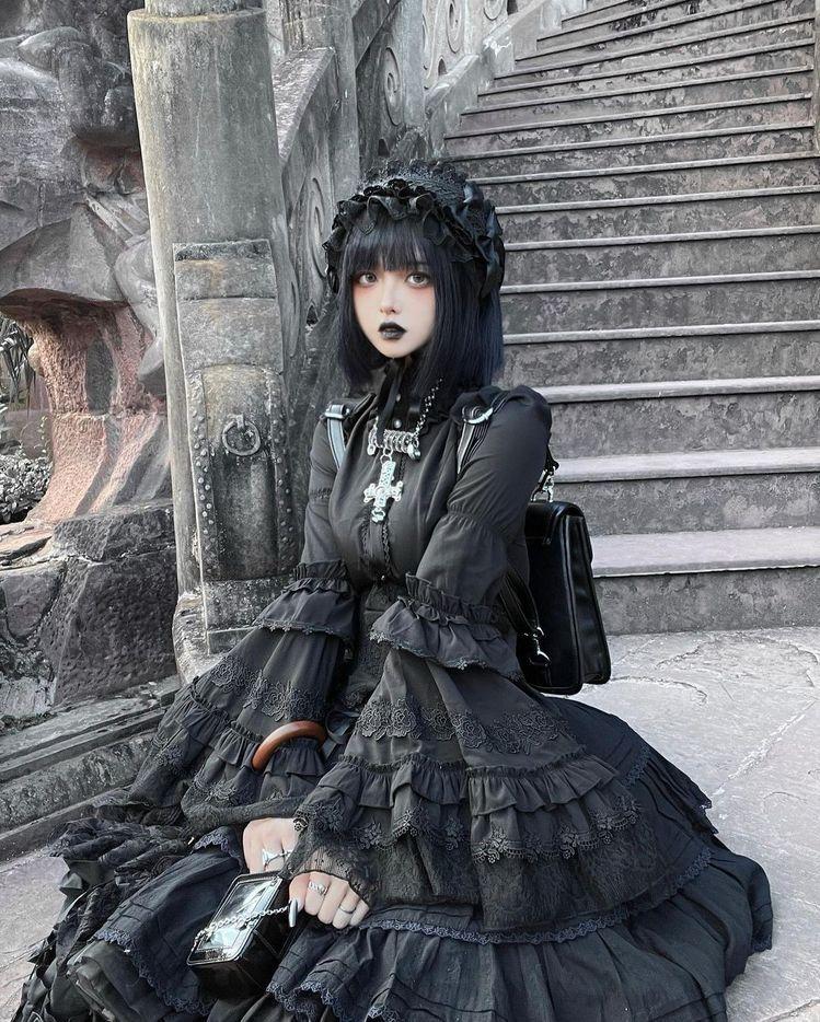 Black Gothic Lolita dress with layered lace and a matching headdress, photographed beside stone steps
