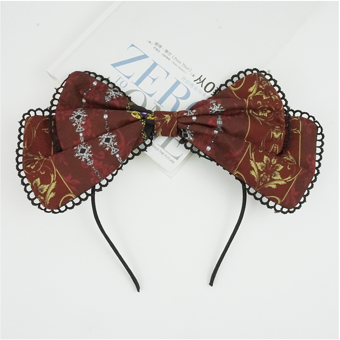 Wine-red bow KC headband with black scalloped lace edging laid flat.