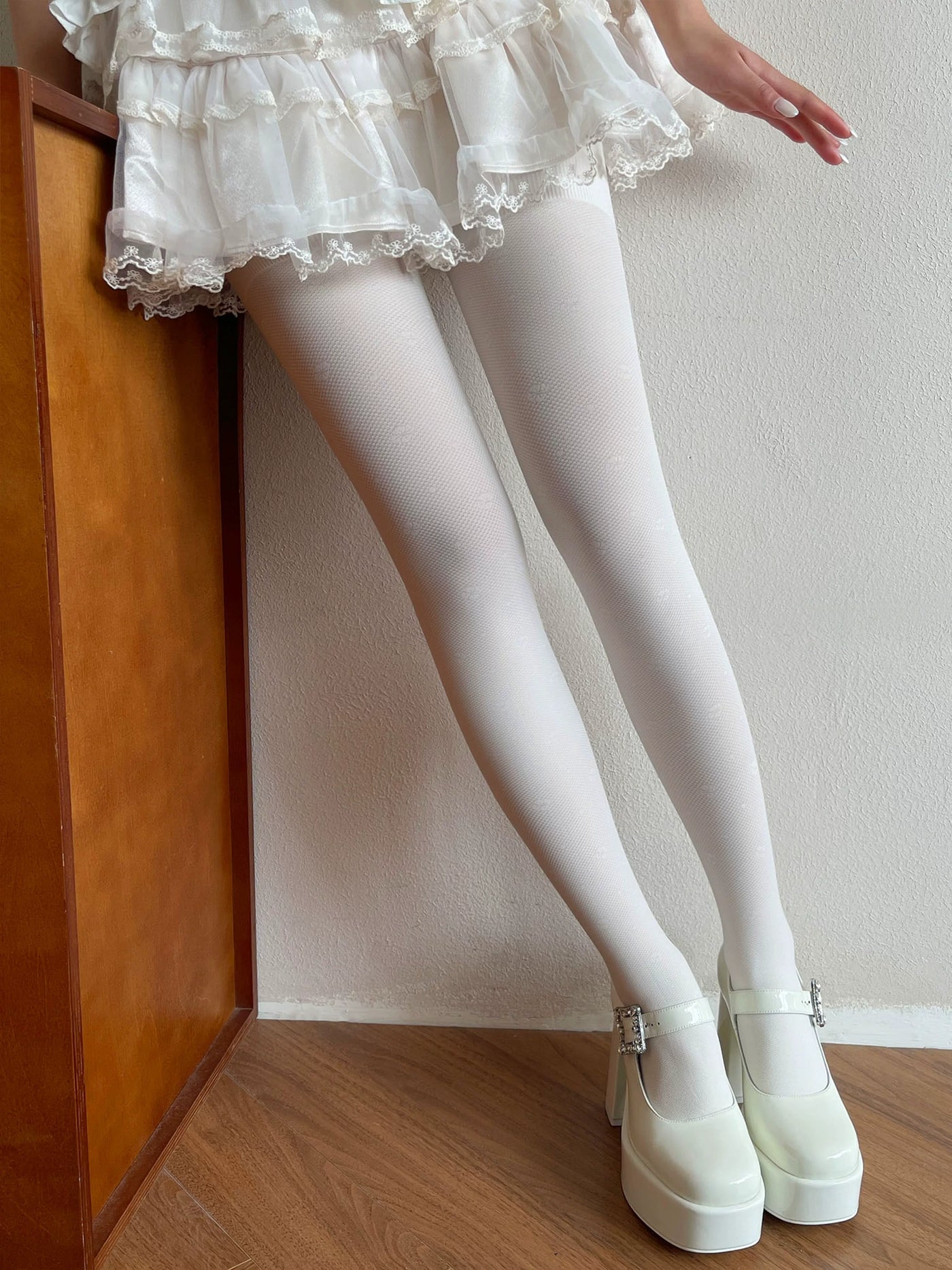 Sock Noble white textured tights styled with a white lace-trimmed skirt and platform shoes
