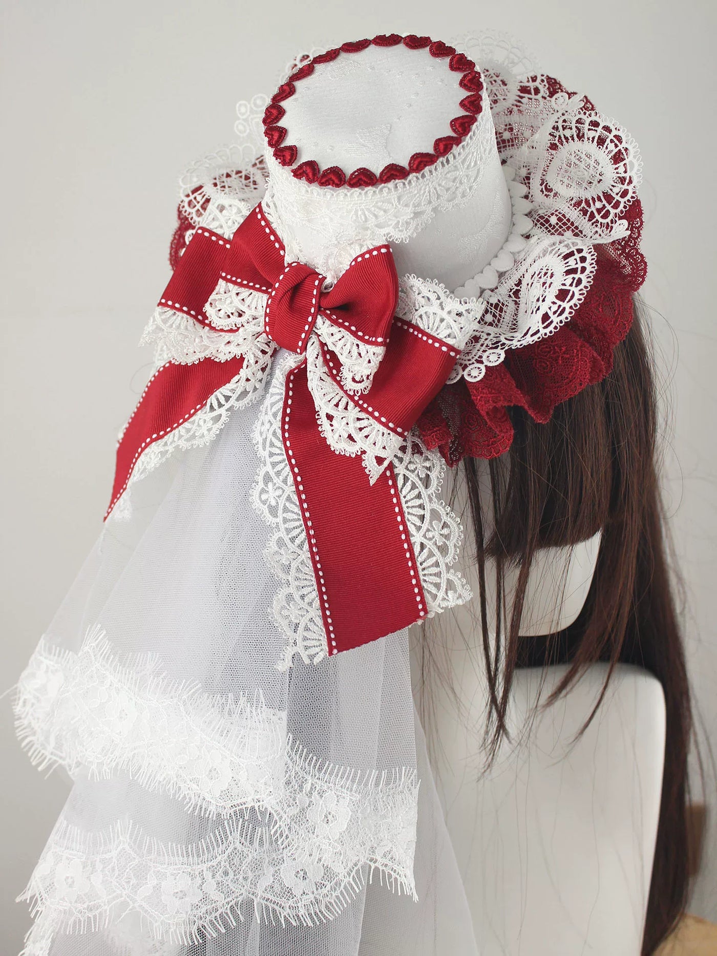Pink, blue and white lace top hats with tulle and bows displayed on wig mannequins.