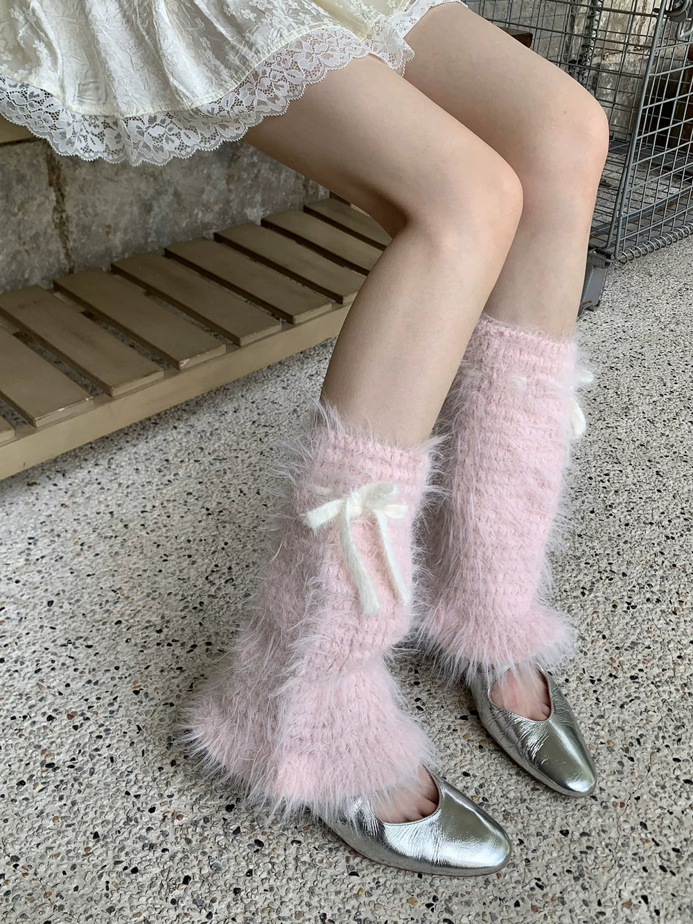 Pink plush mid-calf leg warmers with white tie bows worn over silver pointed shoes.