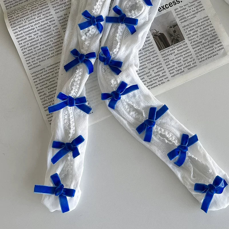 White openwork mid-calf slouch socks with repeated black bow accents styled with a black skirt and platform shoes.