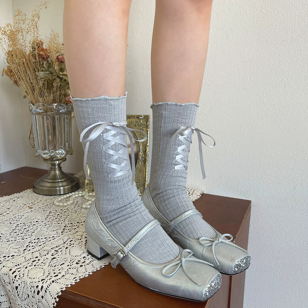 Light gray ribbed slouchy socks with white criss-cross ribbons and silver shoes.