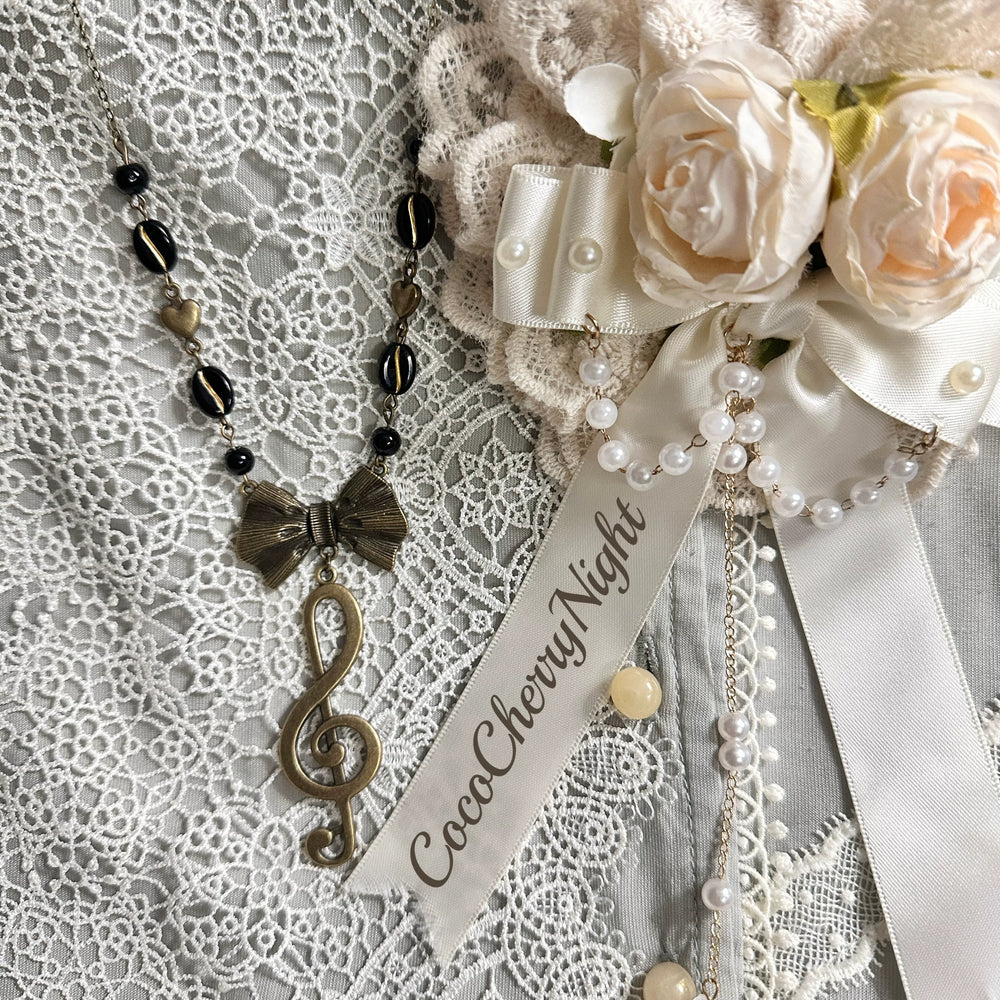 Handmade beaded necklace with black beads, bow, heart accents and treble-clef pendant on lace.