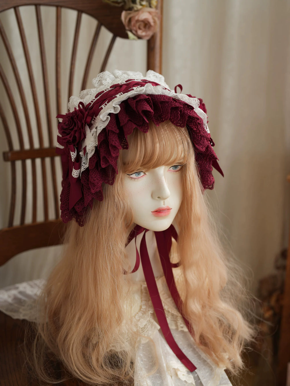 Layered lace bonnet in burgundy and cream tones with long ribbon ties styled on a chair