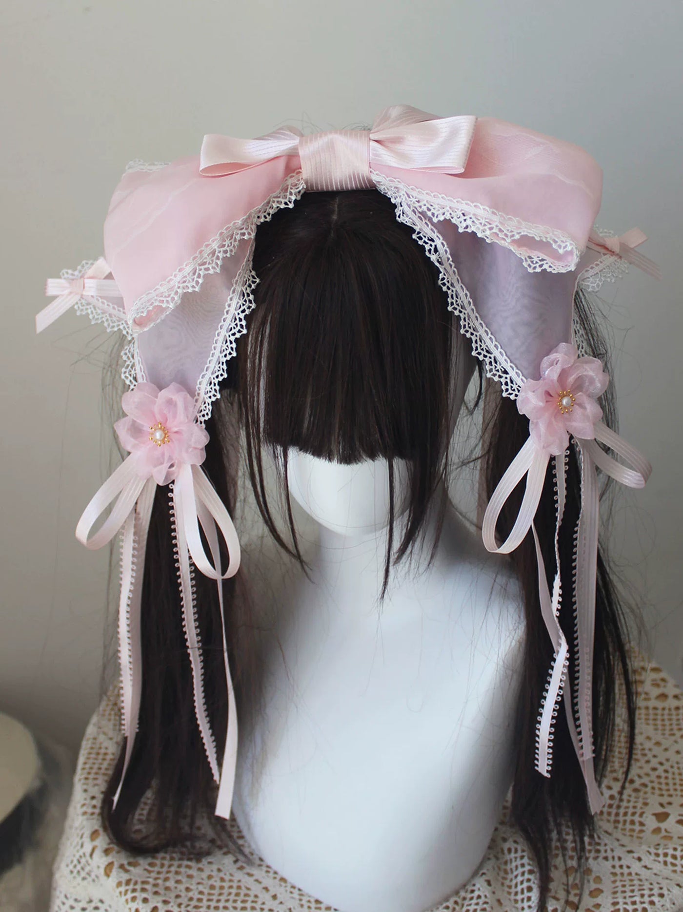 Pink bow headwear with lace-trimmed veil panels and floral ribbon accents on a mannequin