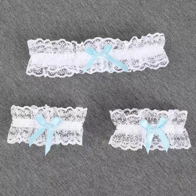 White lace leg garters with blue bows and scalloped trim on a gray background.