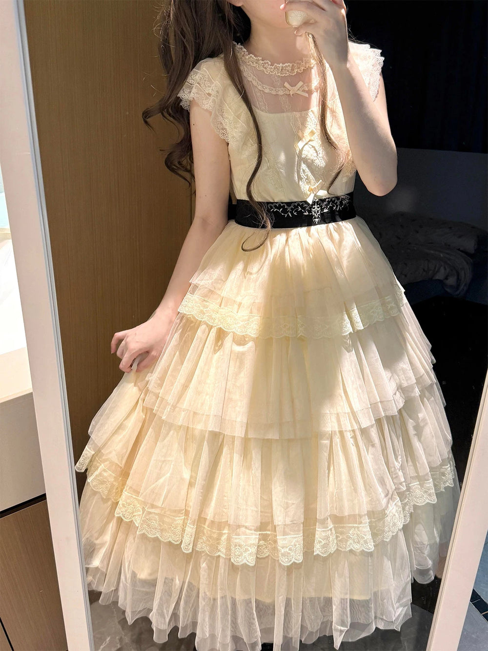 Cream long Lolita OP dress with layered lace ruffles and a black waist belt in a mirror photo.