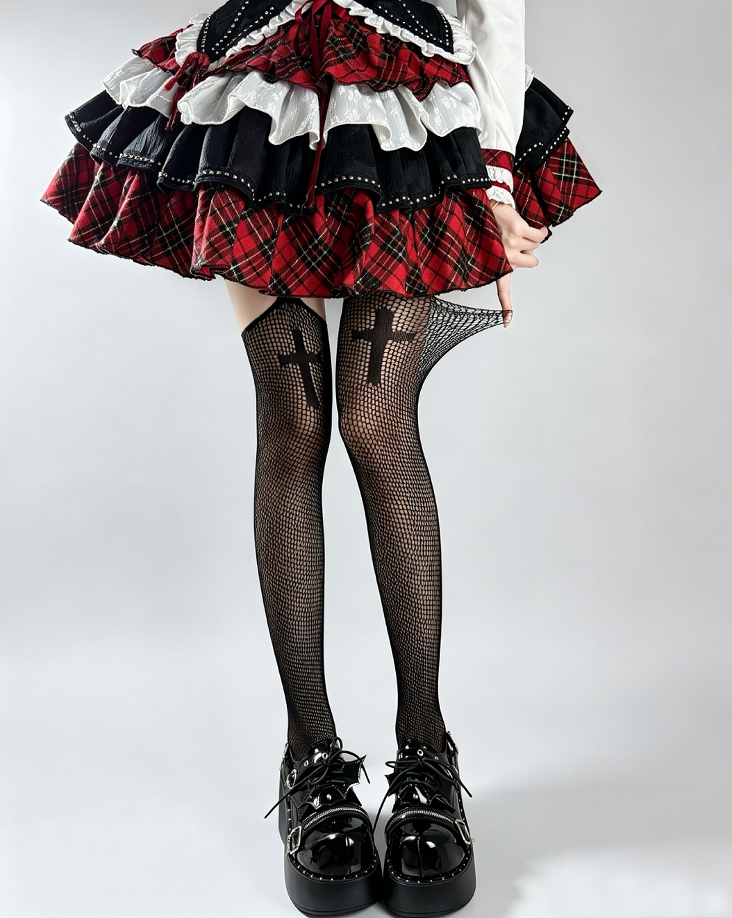 Black fishnet tights with large cross motifs styled beneath a red plaid skirt.