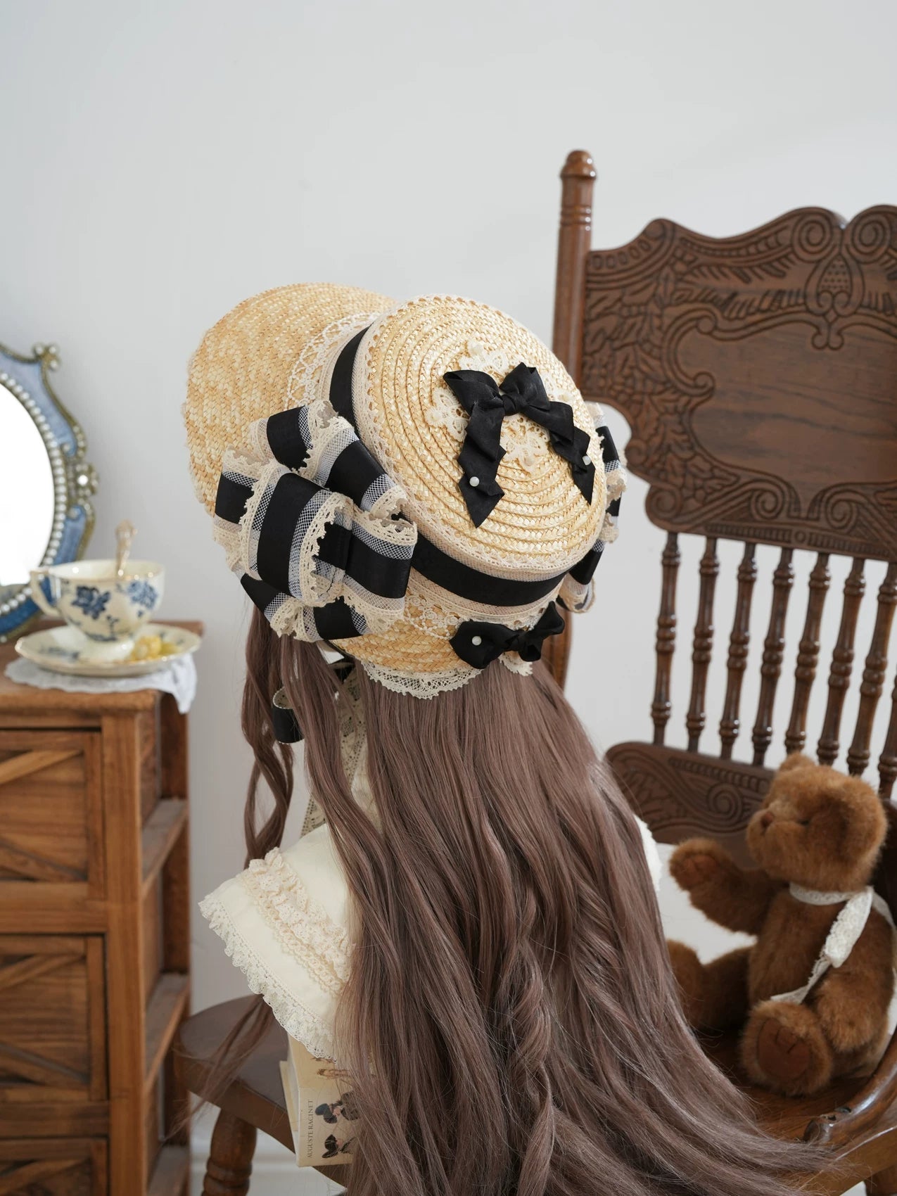 Straw bonnet with a broad lace-trimmed brim and layered black side bow styled on long hair.