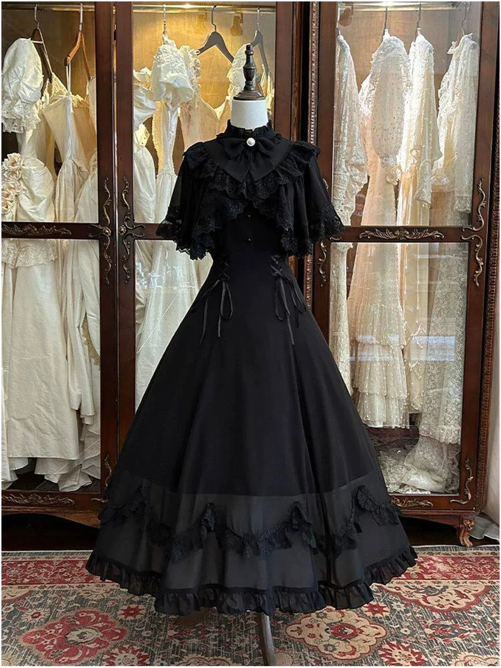 Black long OP dress with lace-trimmed cape sleeves and bow collar on a mannequin.