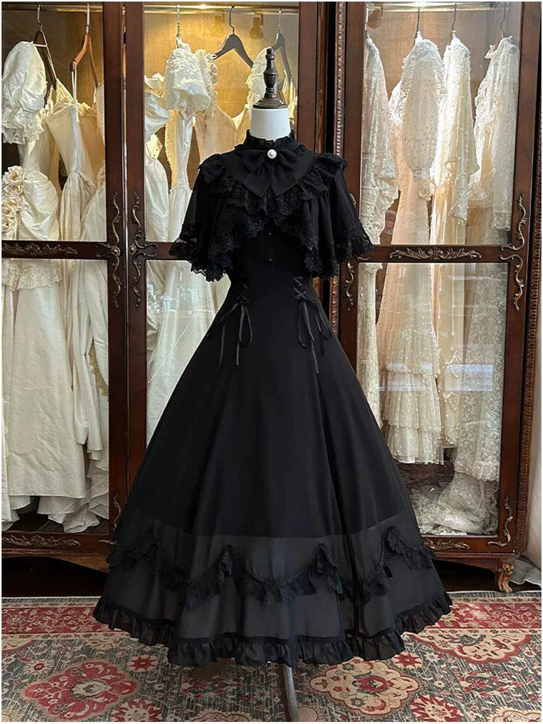 Black long OP dress with lace-trimmed cape sleeves and bow collar on a mannequin.