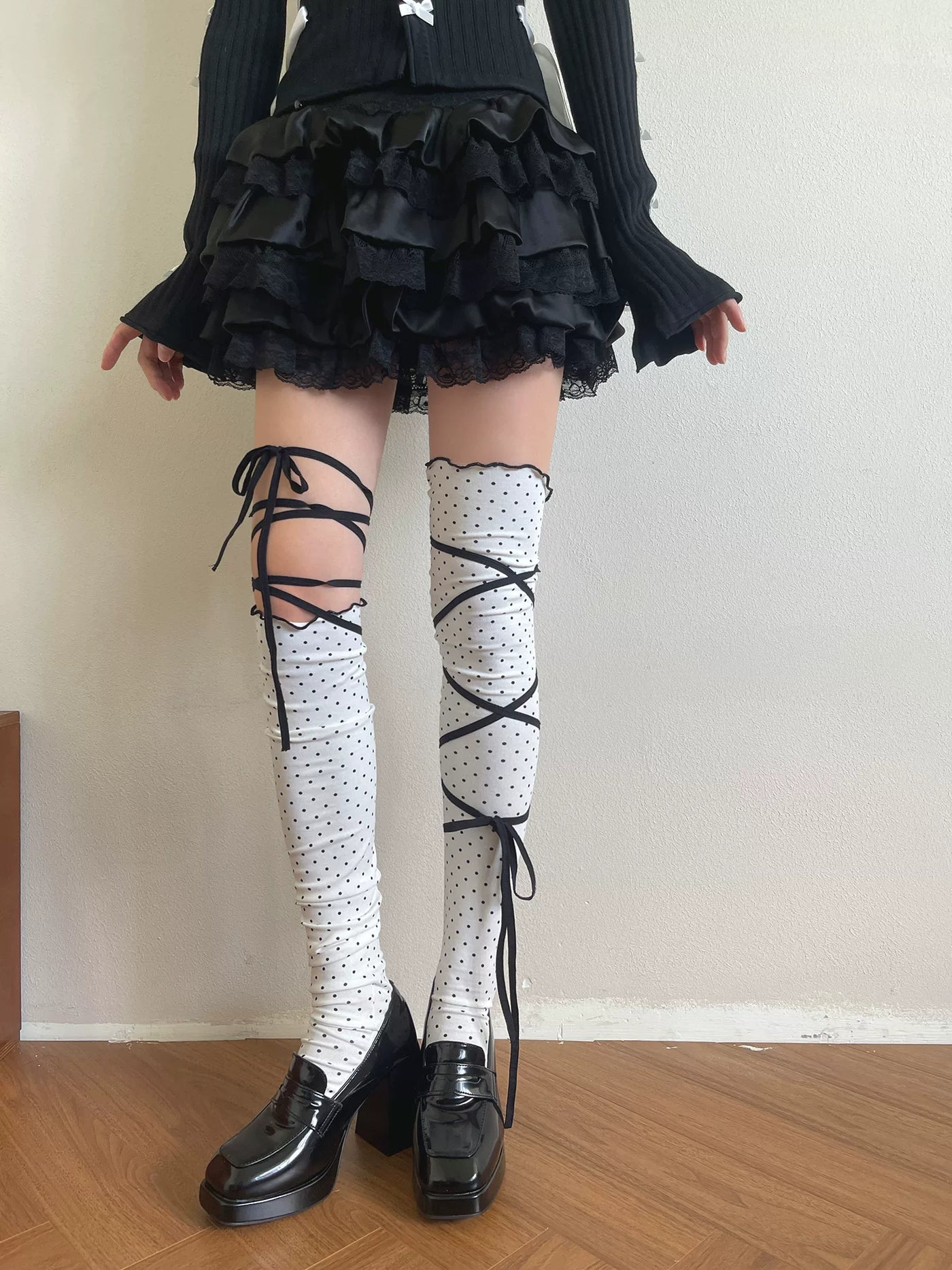 White polka-dot over-the-knee socks with black wraparound ribbons worn beneath a black ruffled skirt