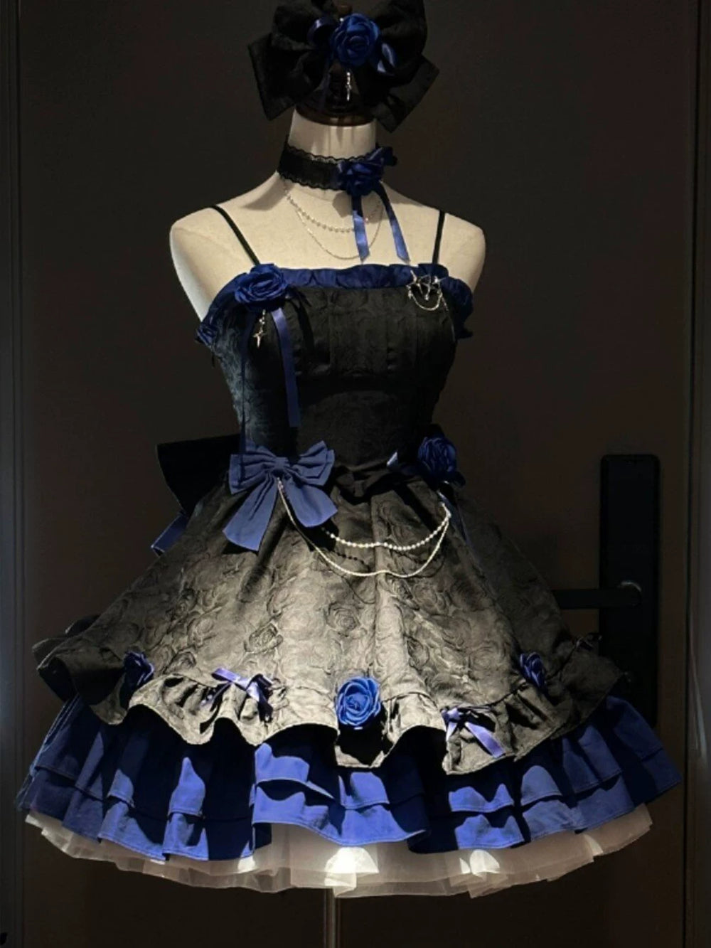 Black and blue Gothic JSK dress with blue roses and tiered ruffles on a mannequin.