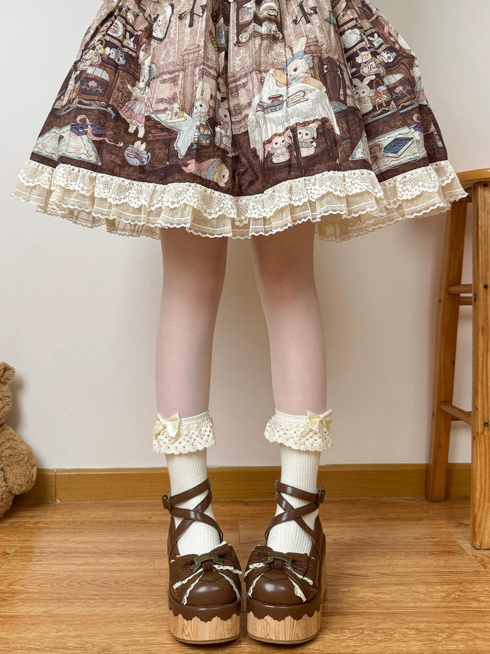 White lace-trimmed mid-calf socks with pale yellow bows styled with a brown illustrated skirt and platform shoes.