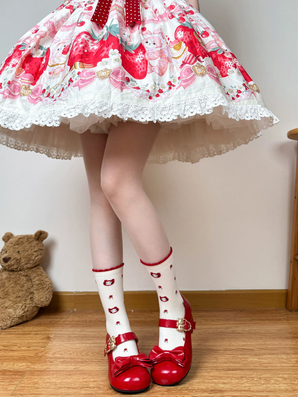 White mid-calf socks with strawberry, cat, floral, and red bow motifs styled with red shoes.