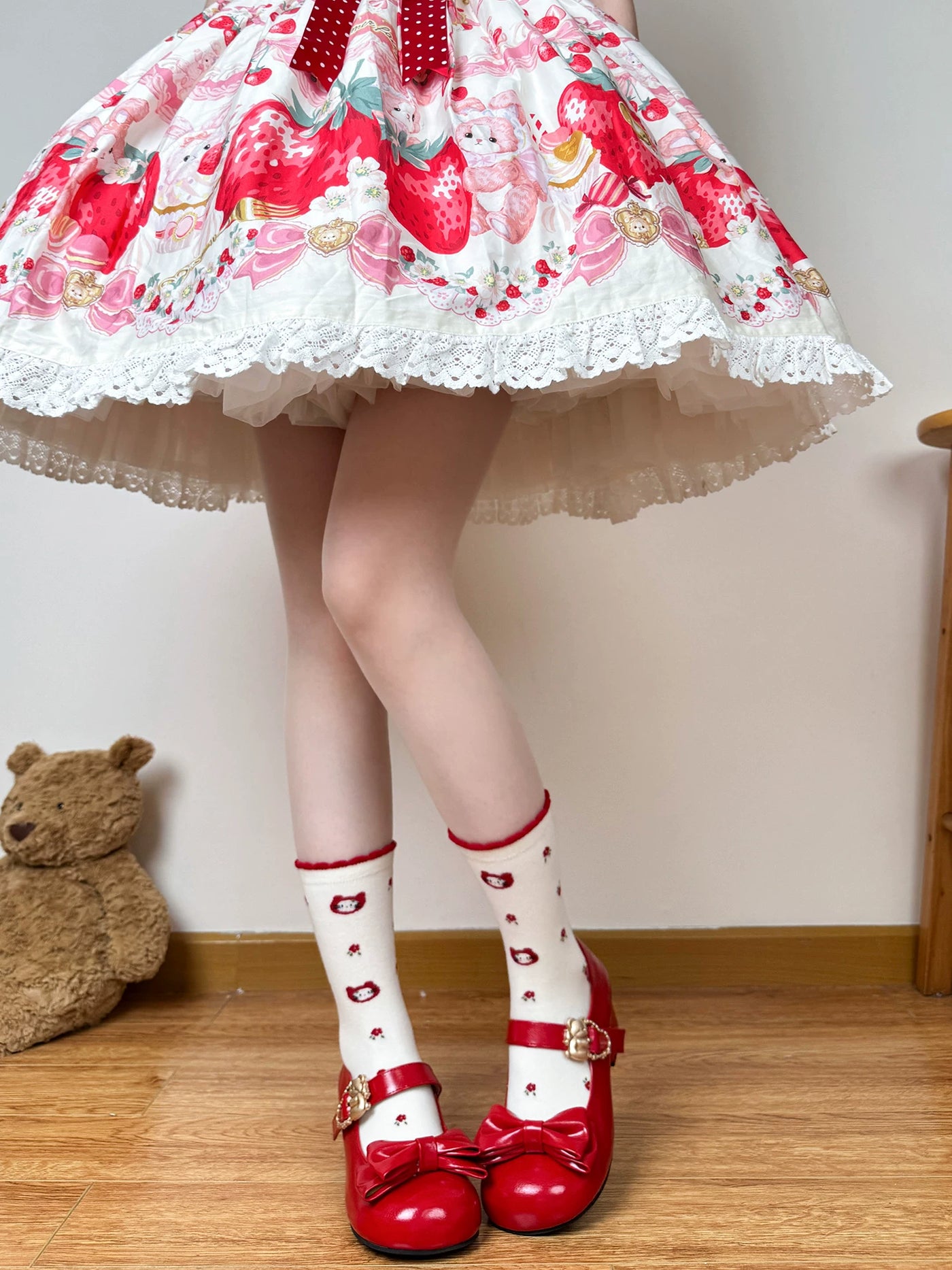 White mid-calf socks with strawberry, cat, floral, and red bow motifs styled with red shoes.