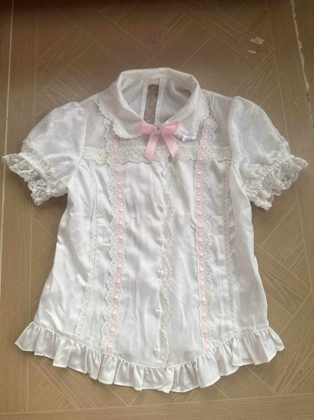 White short-sleeve blouse with rounded collar, lace panels, pink ribbon accents and ruffled hem