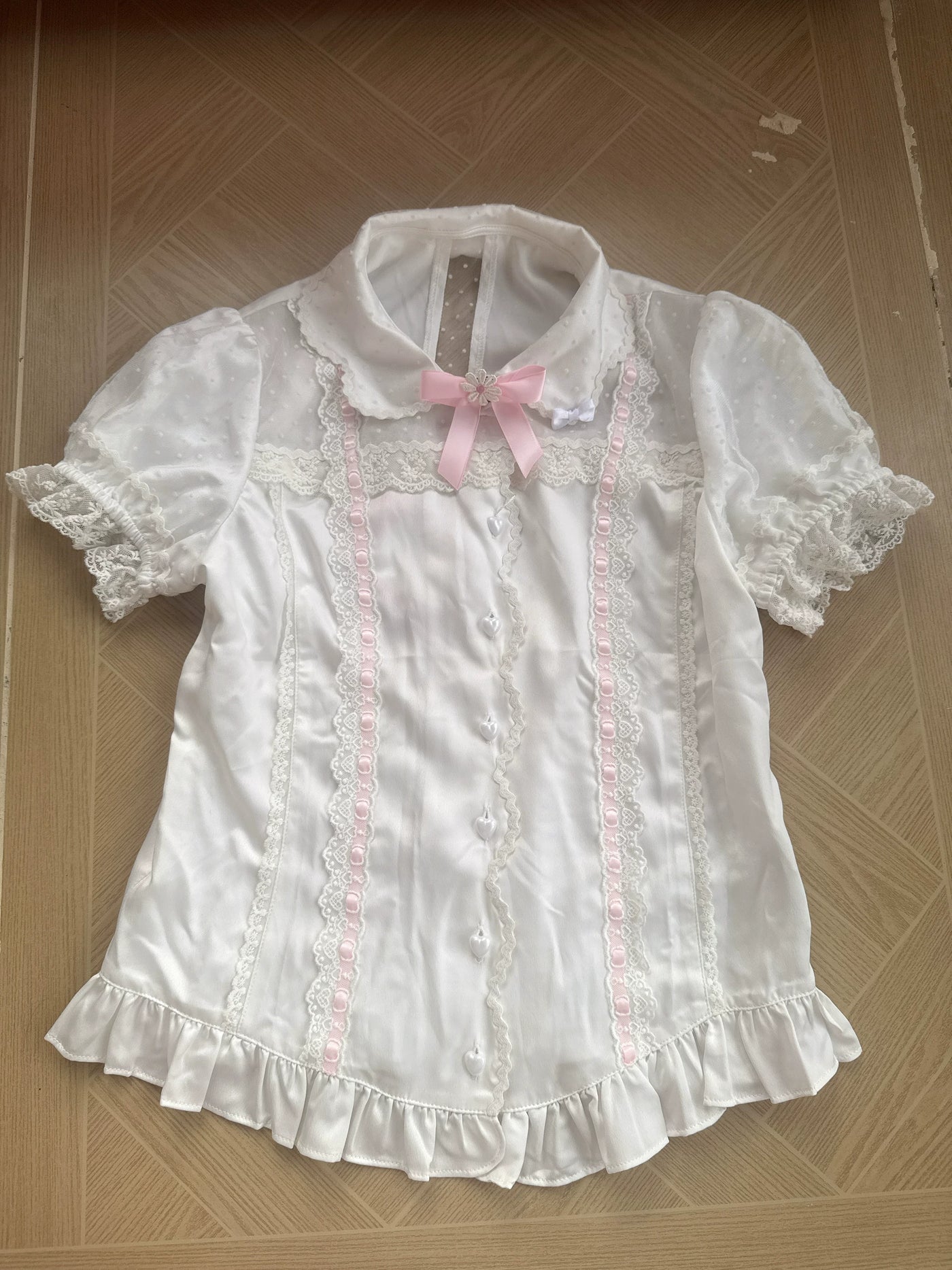 White short-sleeve blouse with rounded collar, lace panels, pink ribbon accents and ruffled hem