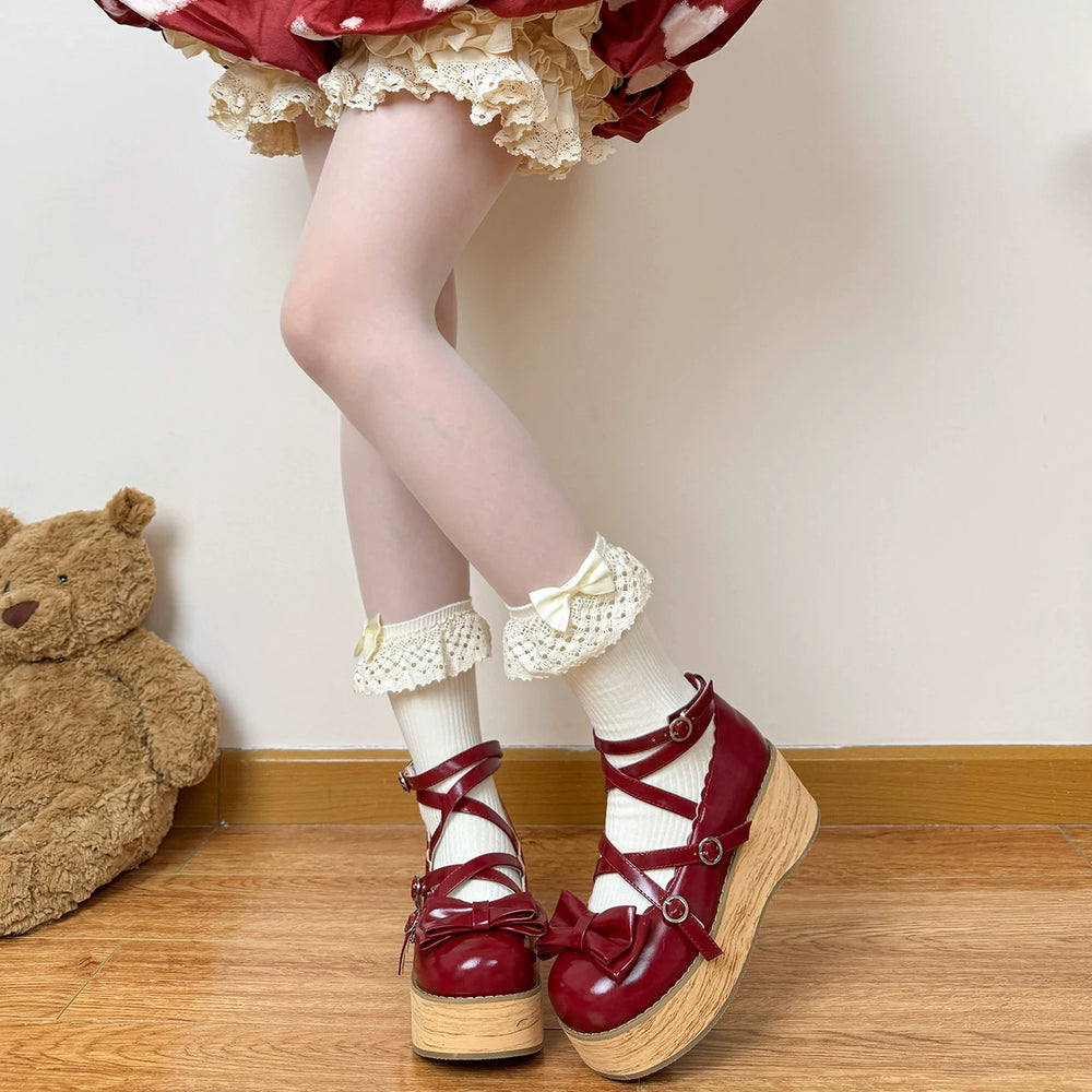 Off-white lace-trimmed slouch socks with pale bows and fluffy pom-poms styled with red platform shoes.