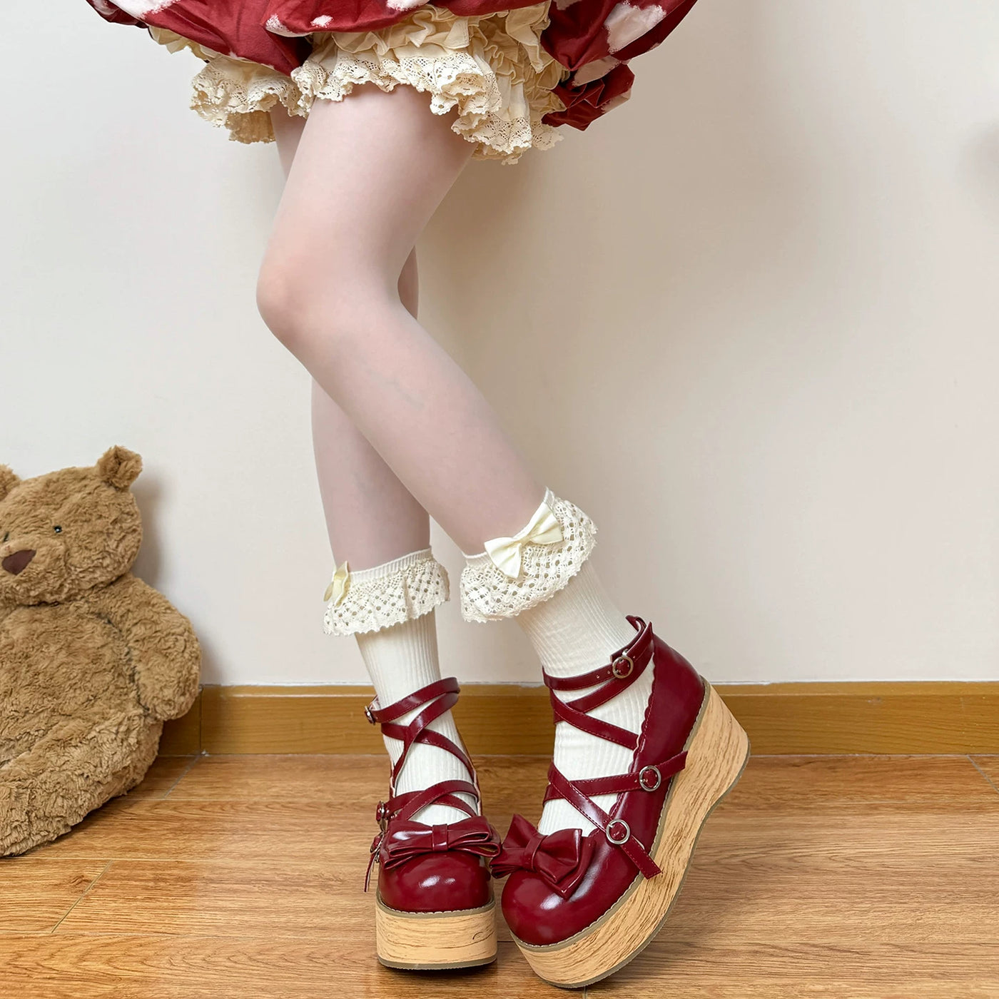 Off-white lace-trimmed slouch socks with pale bows and fluffy pom-poms styled with red platform shoes.