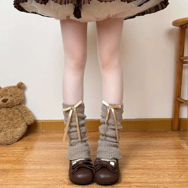 Model wearing thick grey scrunched sock covers with pale ribbon bows.