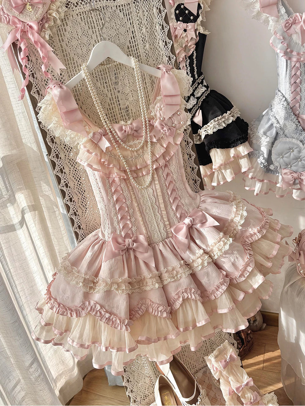 Pink JSK dress with layered ruffles, satin bows, lace trim and a large heart accent on a hanger.