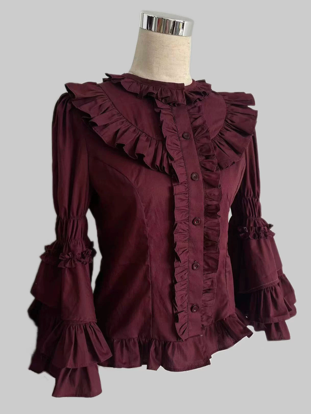Burgundy ruffled blouse with a wide collar and tiered cuffs on a mannequin.
