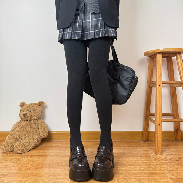 Model wearing dark gray ribbed tights with a pleated plaid skirt and platform loafers.