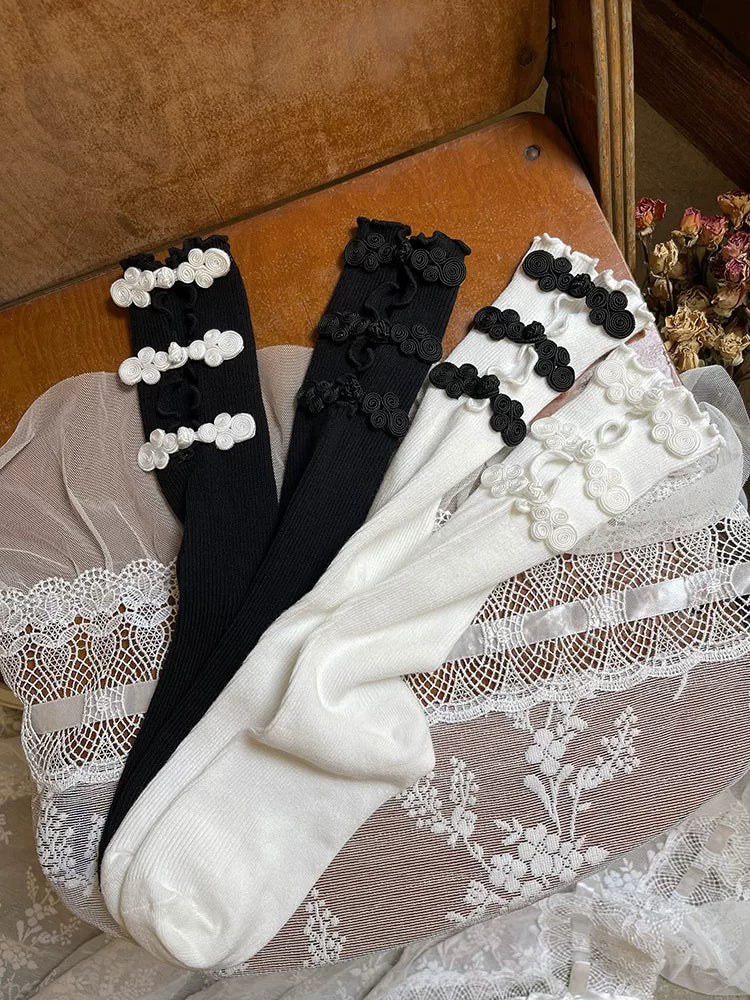 Black and white openwork mid-calf slouch socks with contrasting frog-button details arranged in a flat lay.