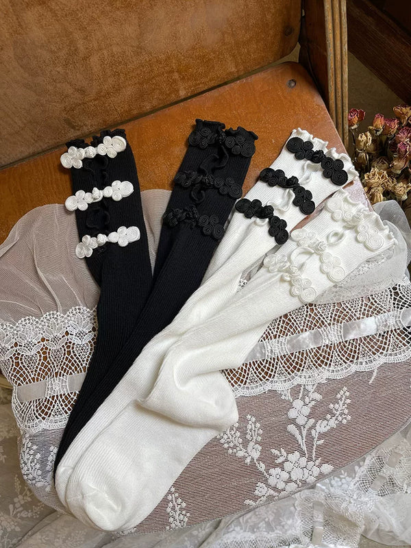 Black and white openwork mid-calf slouch socks with contrasting frog-button details arranged in a flat lay.