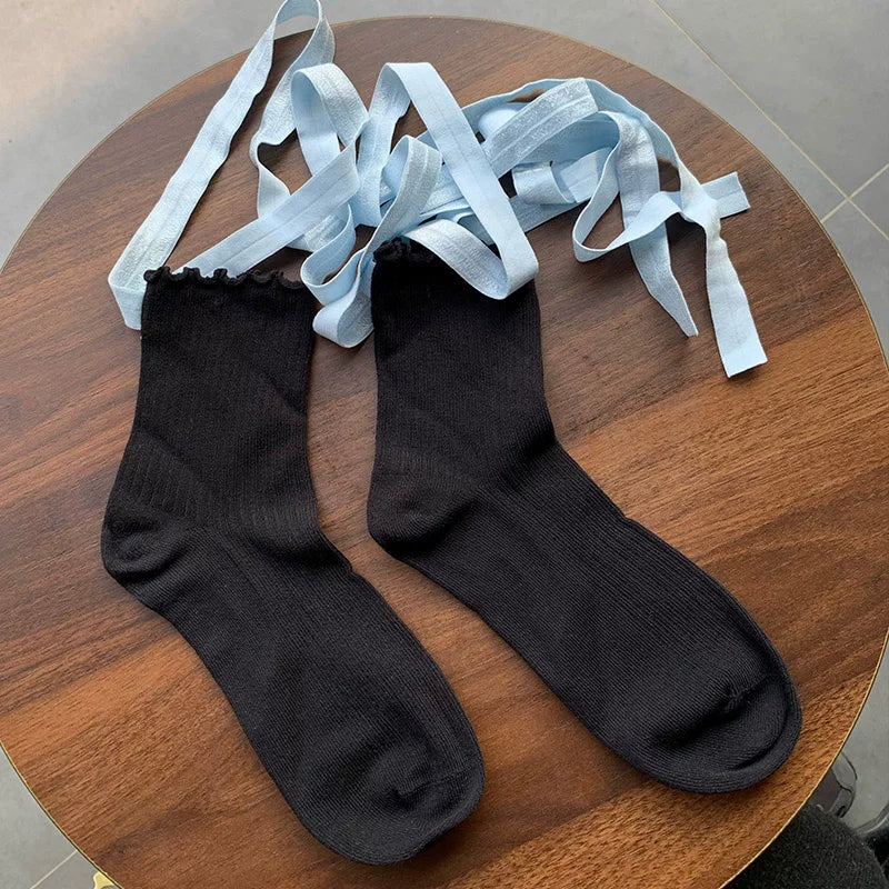 Pair of black calf socks with pale blue tie straps displayed on a wooden table.
