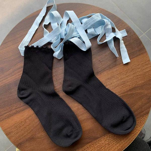 Pair of black calf socks with pale blue tie straps displayed on a wooden table.