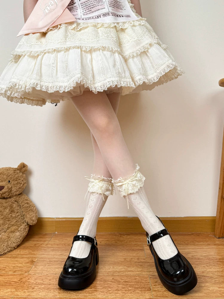White openwork mid-calf socks with lace cuffs and bows styled with black Mary Jane shoes.