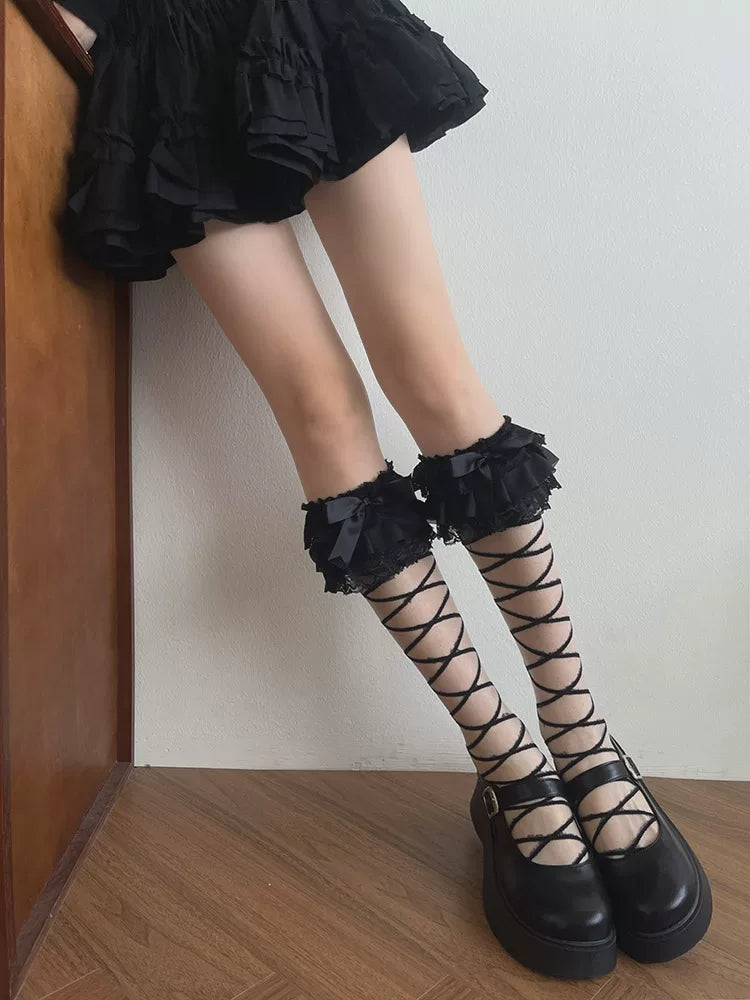 Black mid-calf scrunch socks with lace cuffs, bows and diagonal ribbon straps styled with Mary Jane shoes.