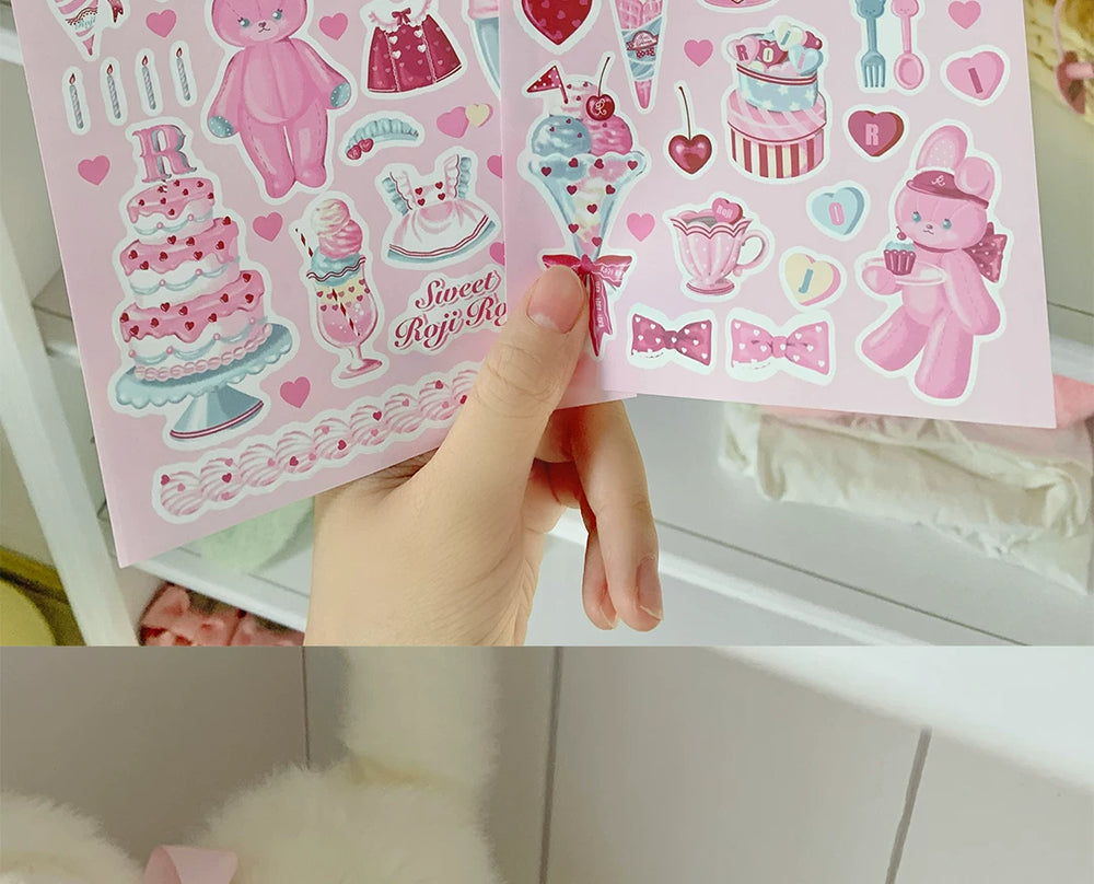 Two pink PE sticker sheets with dessert, tea, bunny, heart and ribbon motifs held by hand.