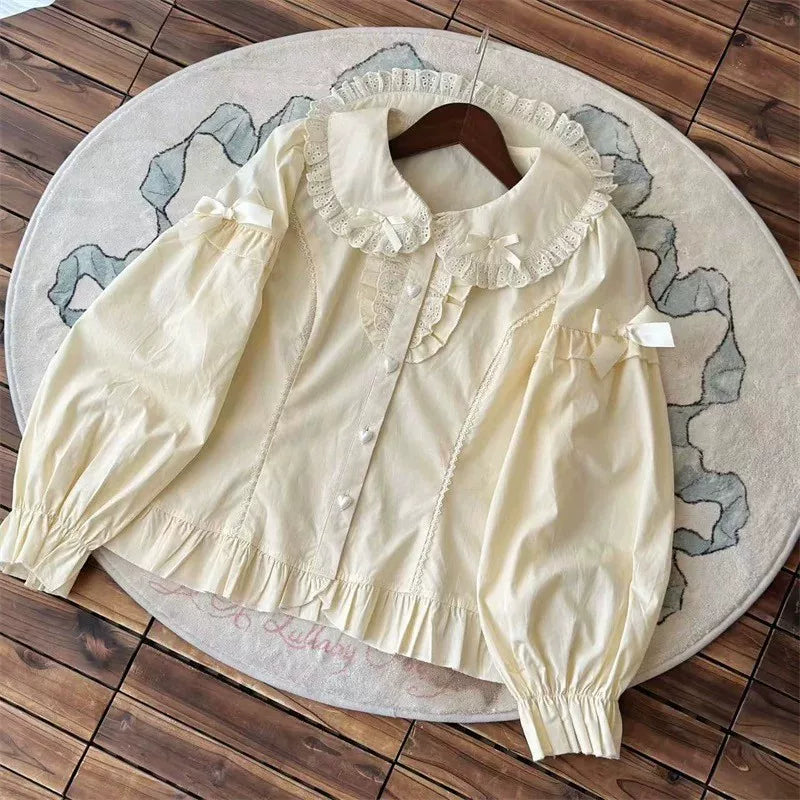 Cream long-sleeve blouse with lace Peter Pan collar and ruffled hem laid on a rug