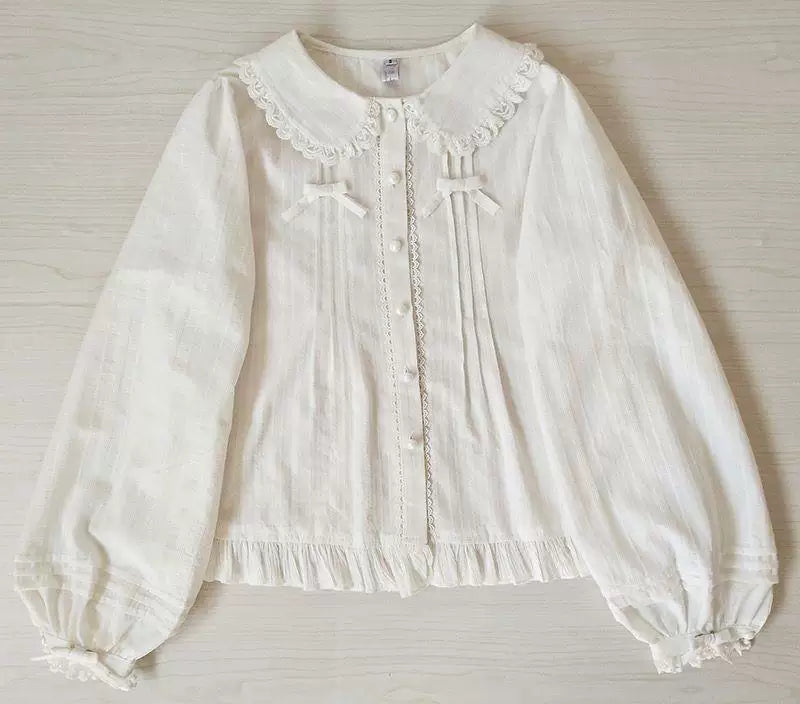 White long-sleeve blouse with lace collar, front bows, gathered cuffs, and ruffled hem on a mannequin